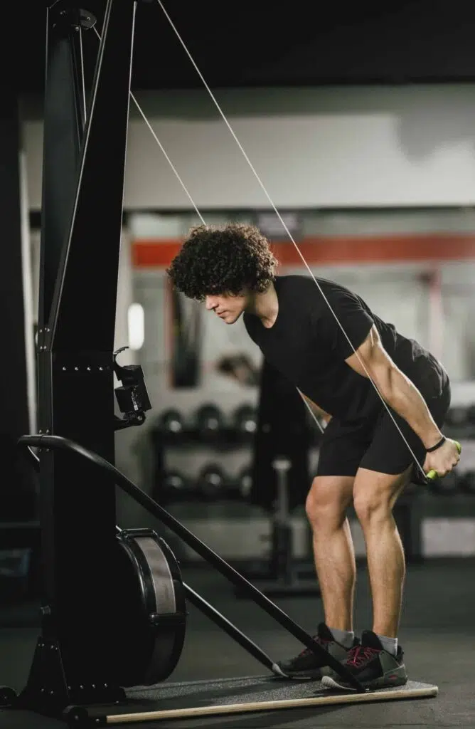 Athlète utilisant un SkiErg en salle : bras tendus vers le haut puis tirage des poignées vers le bas, position debout légèrement fléchie