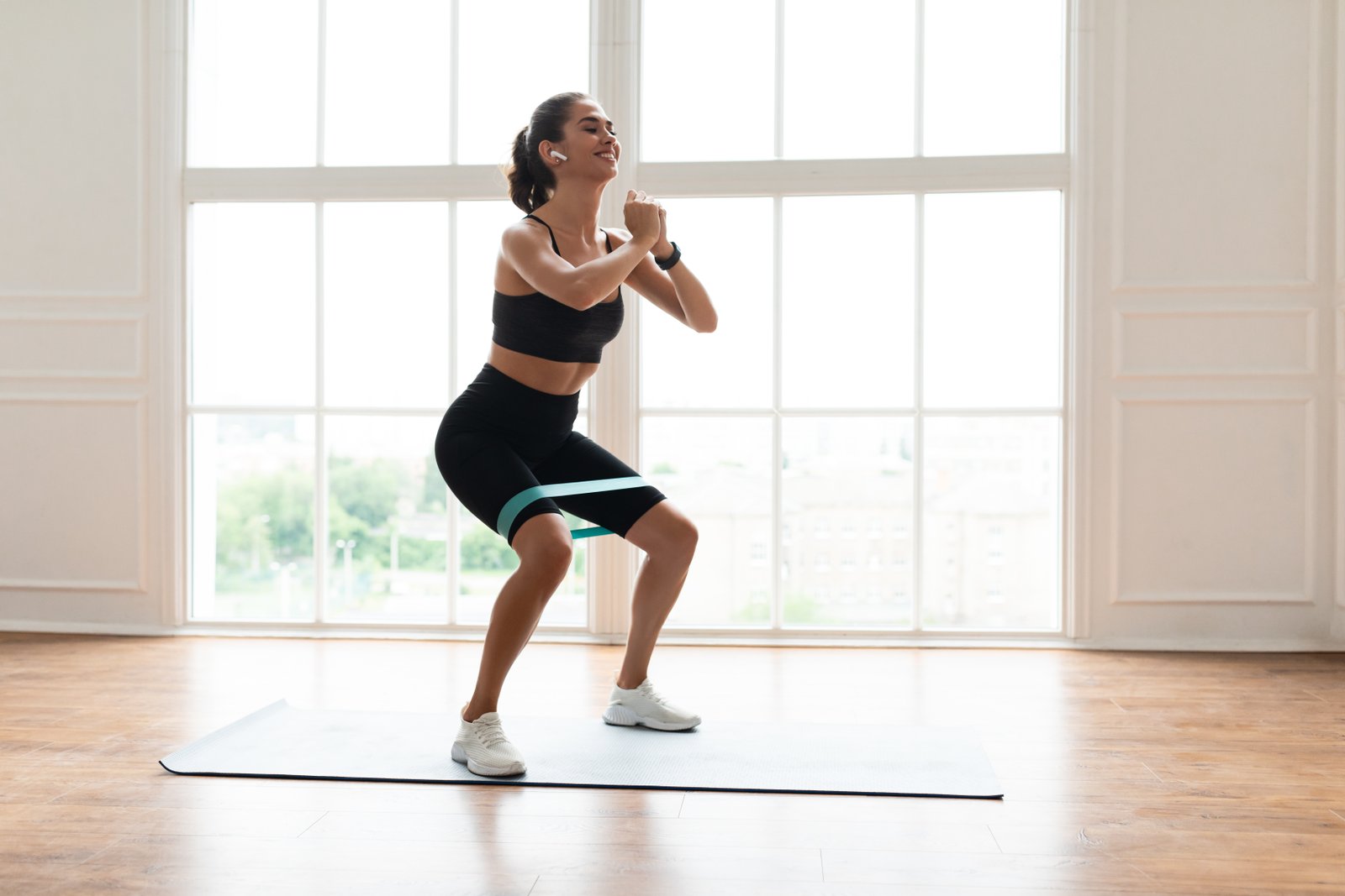 Exécution du squat avec élastique : bande placée au-dessus des genoux, pieds écartés pointes vers l'extérieur, genoux poussés vers l'extérieur, dos droit et cuisses parallèles au sol
